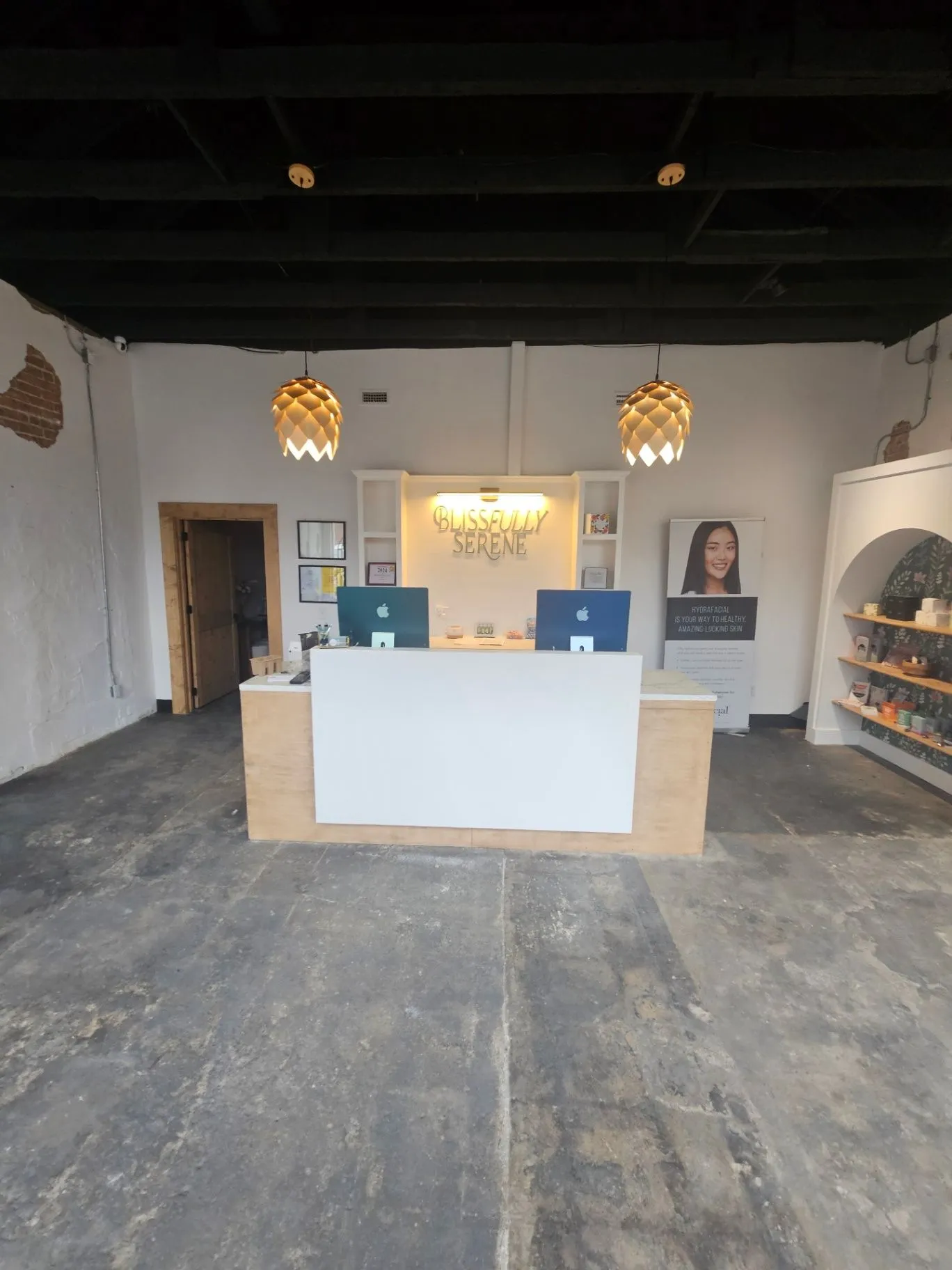 Completed spa reception with a white desk, pendant lights, and illuminated Blissfully Serene sign